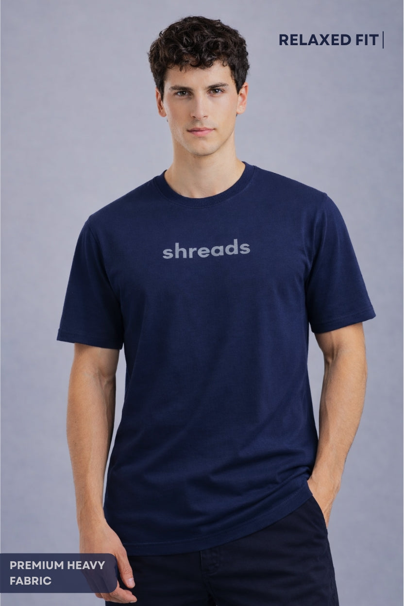 Man wearing a shreads plain navy blue t-shirt o relaxed fit not oversized with 'shreads' logo on a gray background